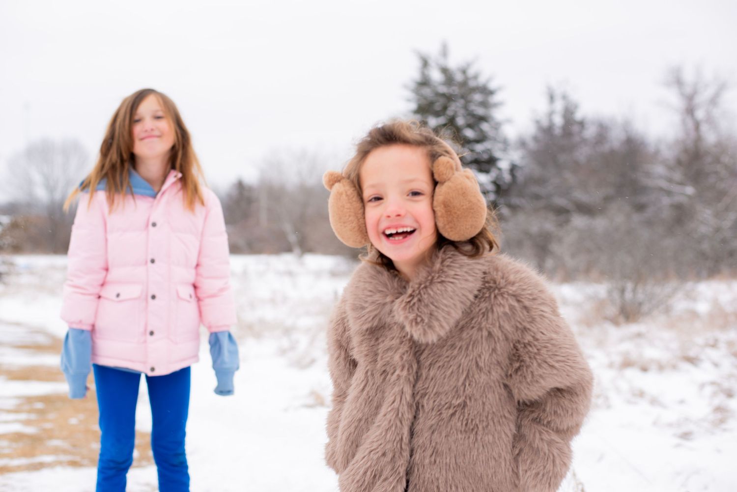 Two people enjoying a snowy winter day outdoors, wearing warm coats with one in pink and another in brown.