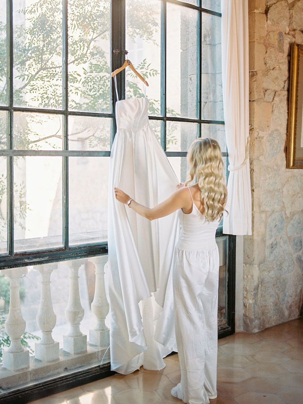 White wedding gown displayed against sunlit windows in a stone villa.