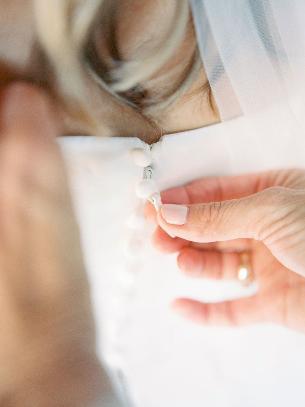 Close-up of hands fastening delicate buttons on white fabric.