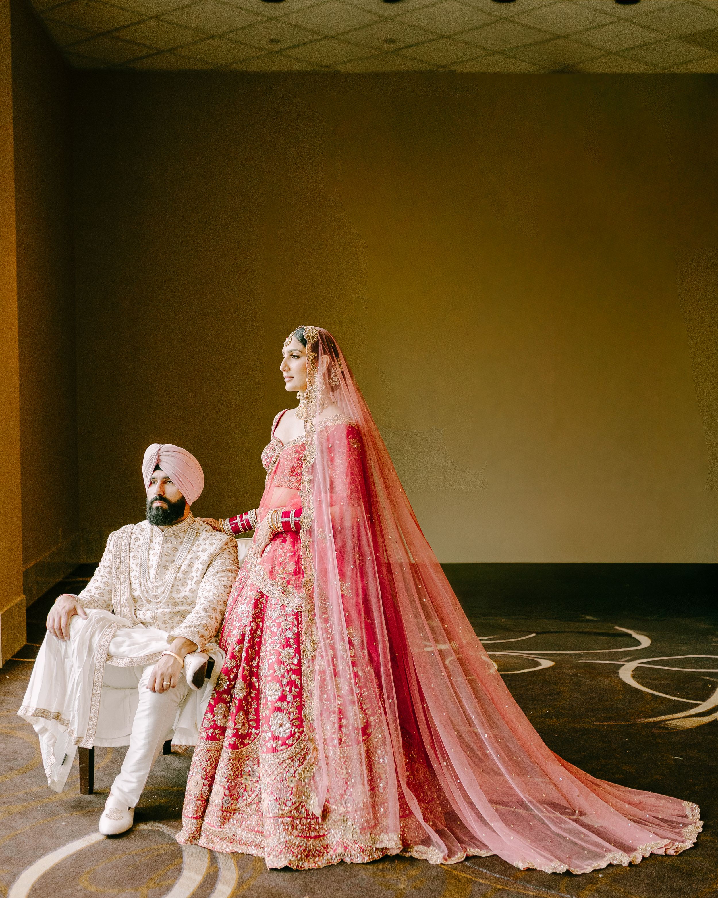 Traditional Sikh wedding couple in ornate pink and white ceremonial attire.