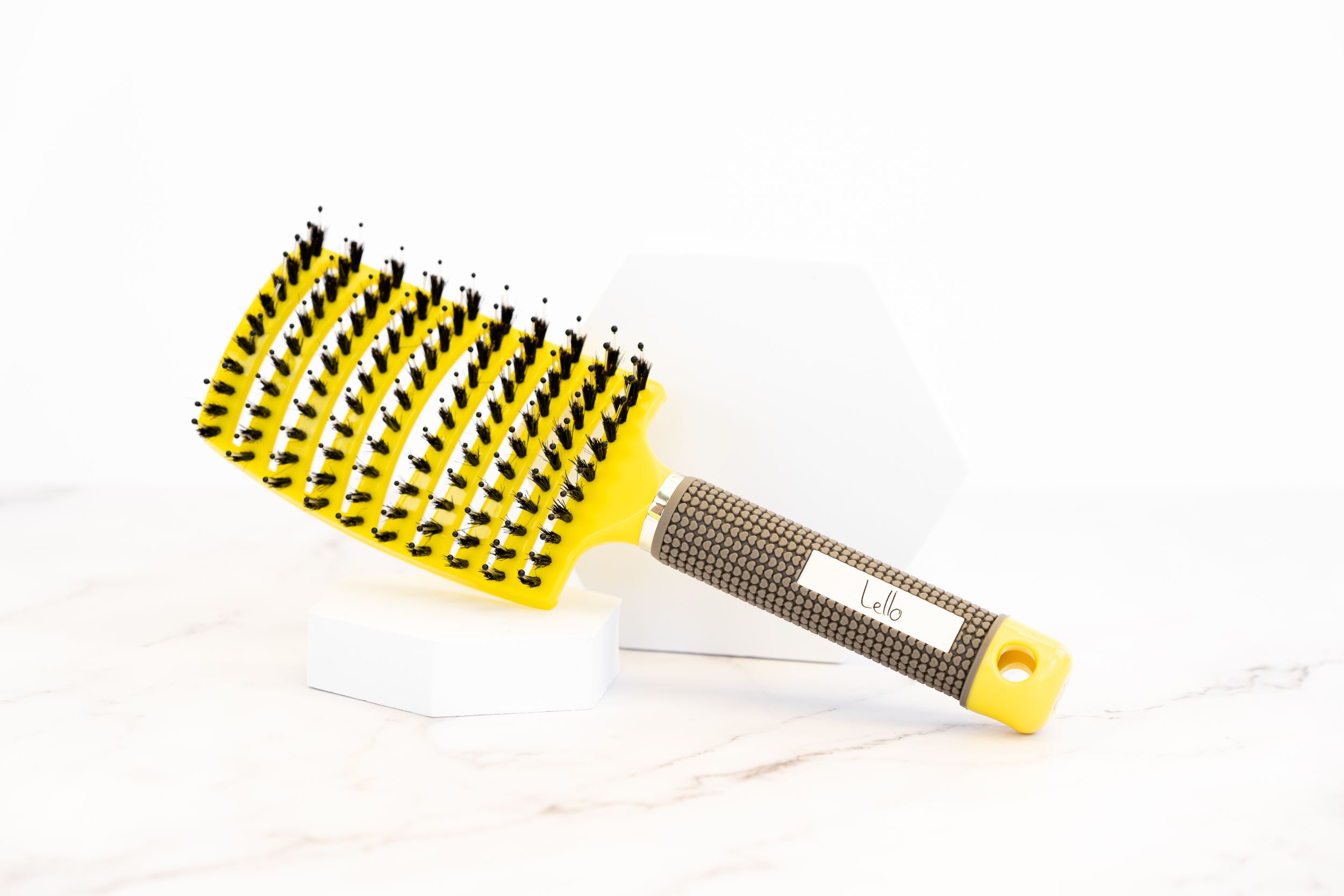 Yellow and black curved bristle hairbrush with ergonomic handle on white surface.