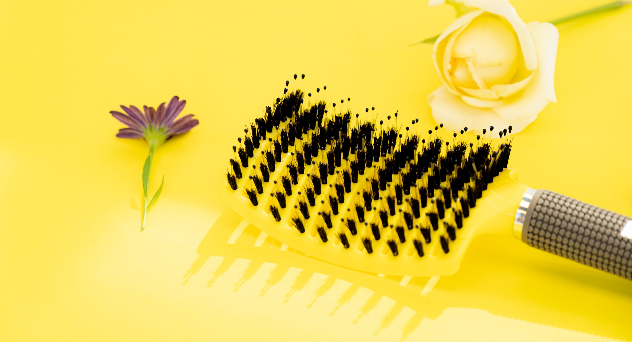 Hair brush with black bristles on yellow background with flower decorations.