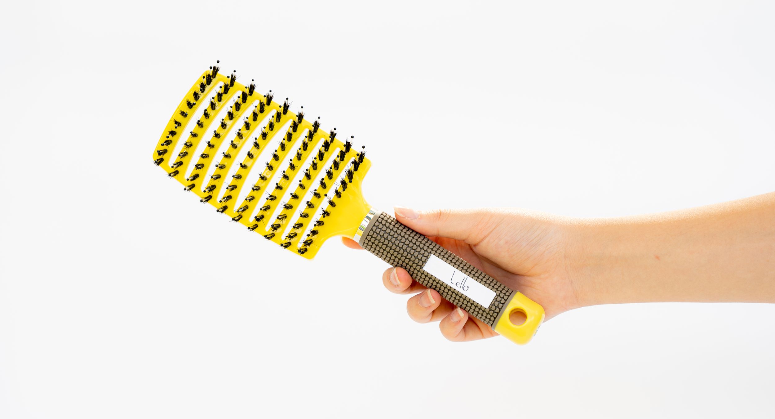 Hand holding yellow and black styling brush against white background.