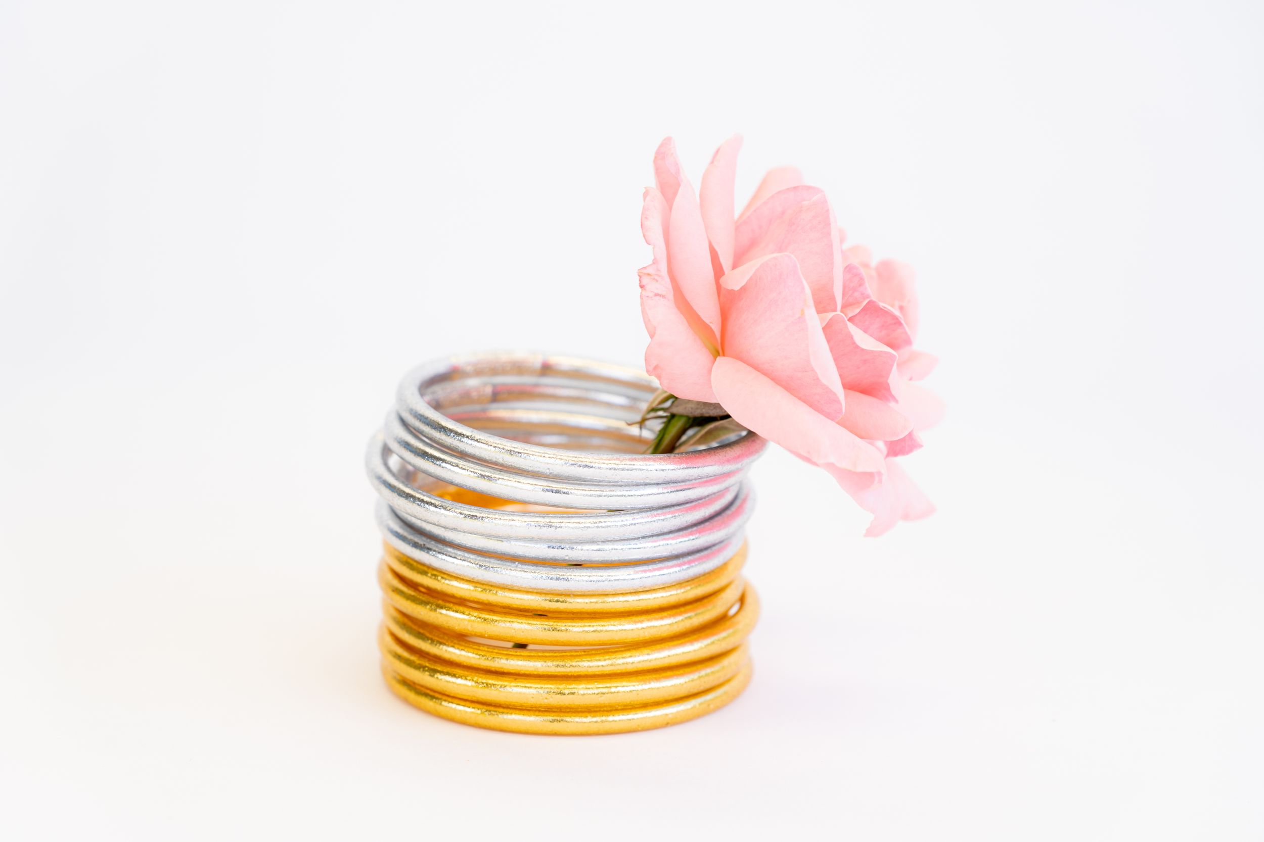 Stack of metallic silver and gold bangles with pink flower decoration.