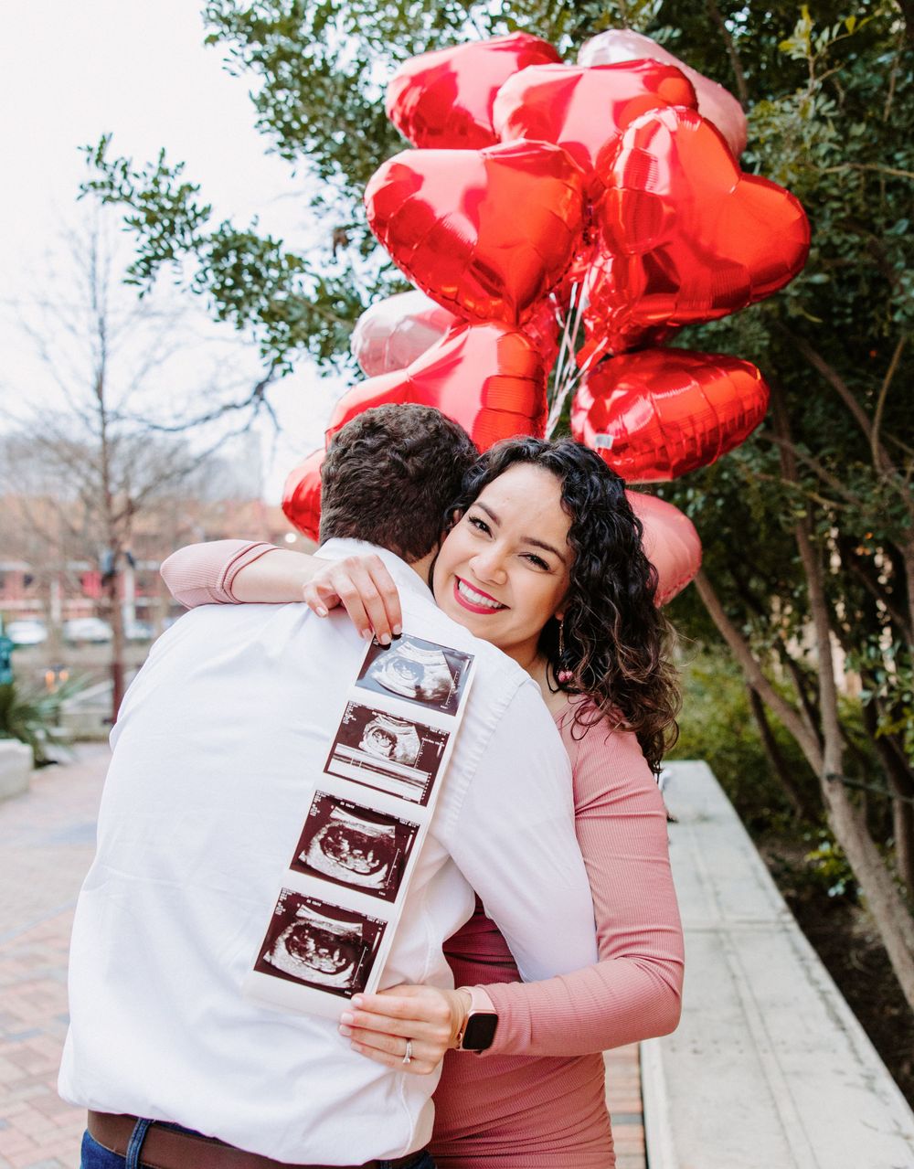 San Antonio Maternity Photography. A couple embraces while holding red heart balloons and displaying ultrasound photos.