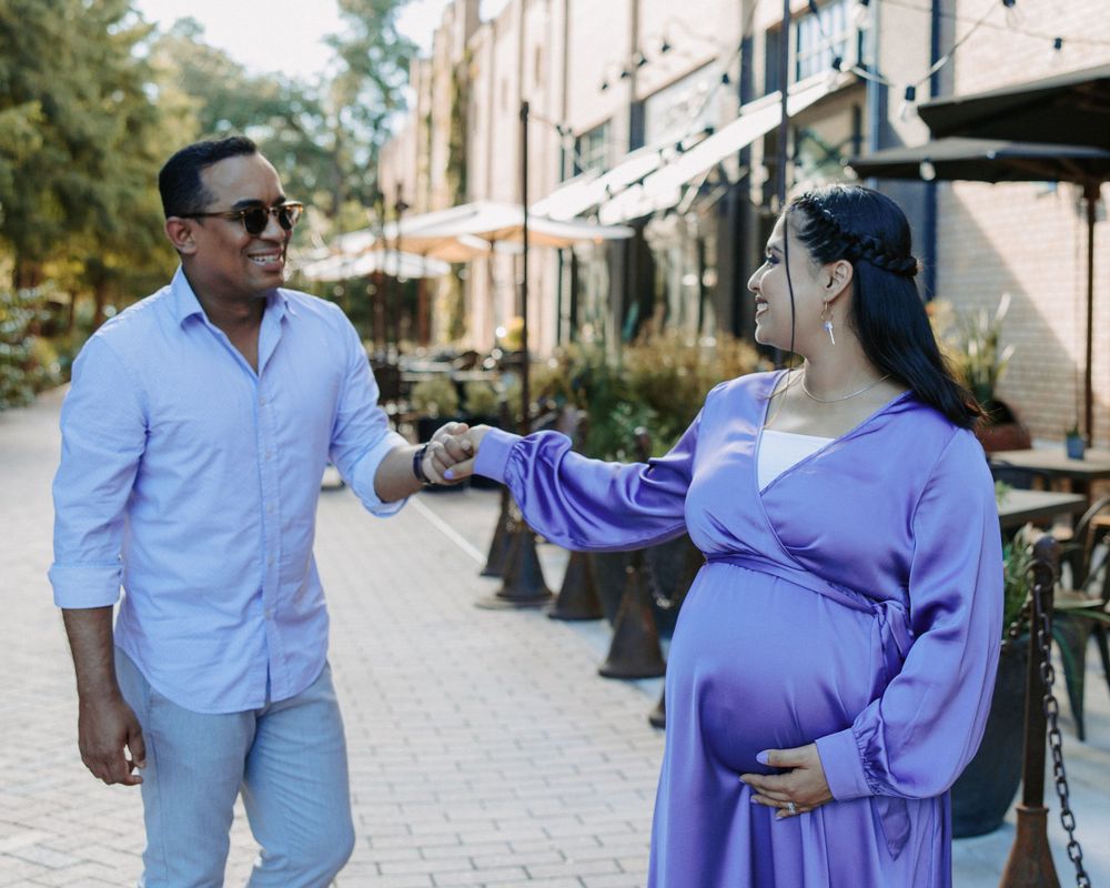 San Antonio Maternity Photography. A couple in coordinating outfits poses playfully on an urban sidewalk.