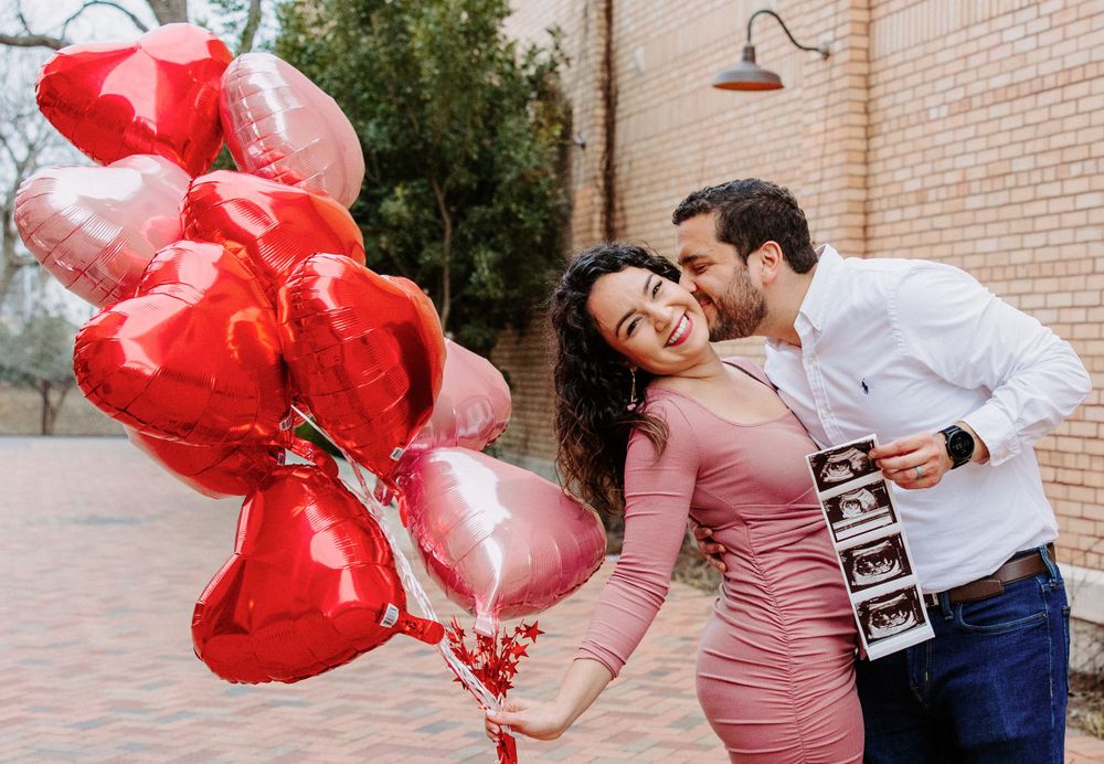 San Antonio Maternity Photography. A couple shares an intimate moment on a brick pathway with red heart balloons.