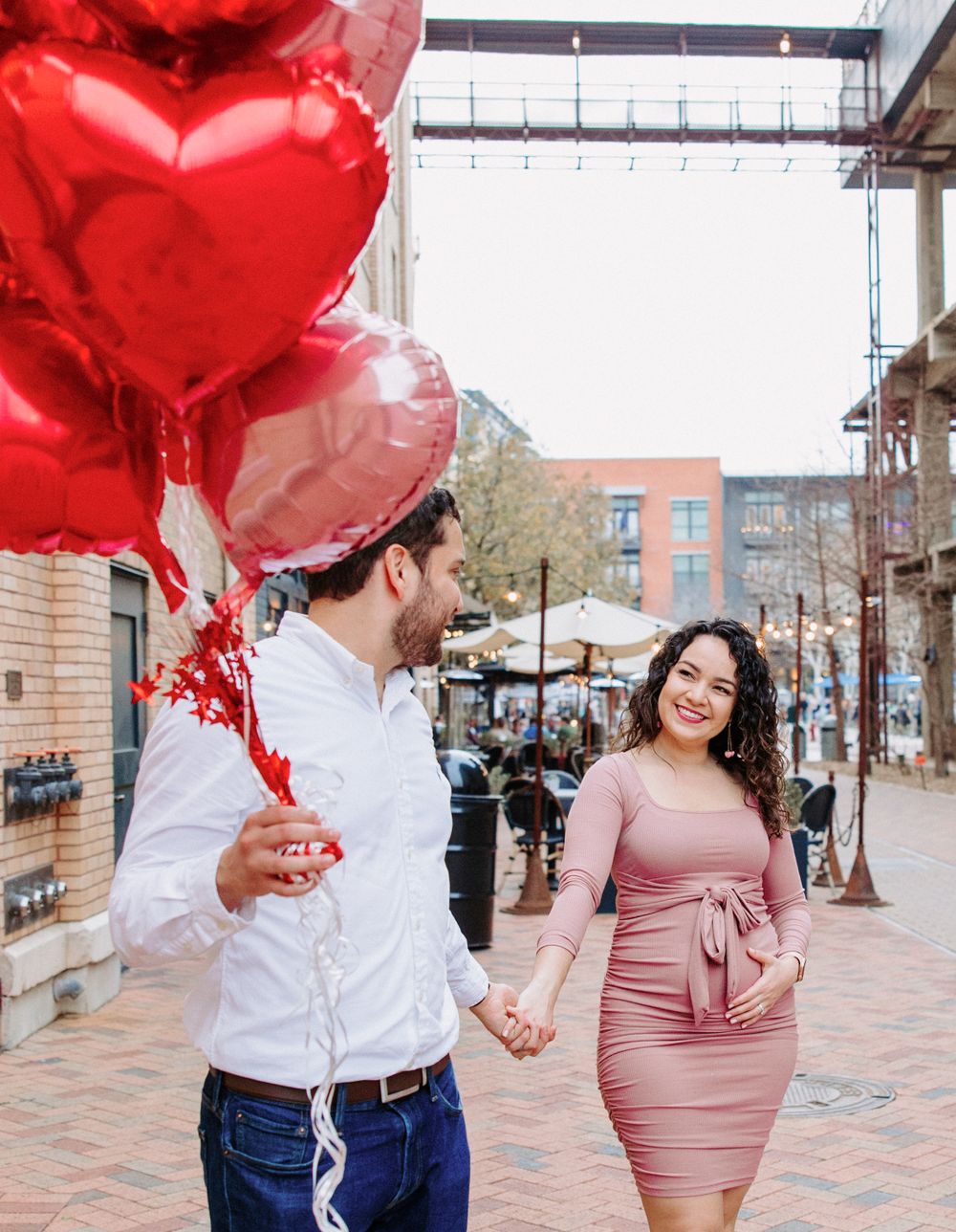 San Antonio Maternity Photography. A couple walks on a brick sidewalk, with red heart-shaped balloons creating a romantic atmosphere.