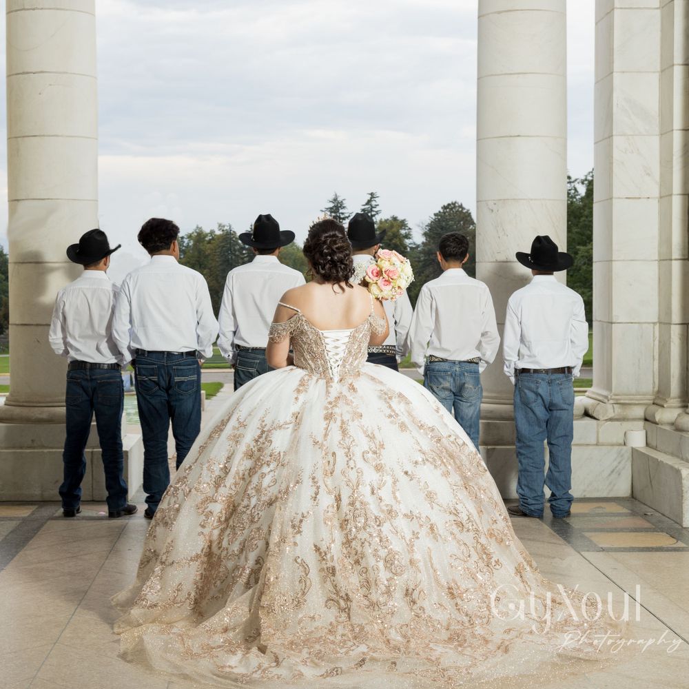 Back view of a quinceañera in a detailed ballgown with attendants in matching white shirts and cowboy hats.