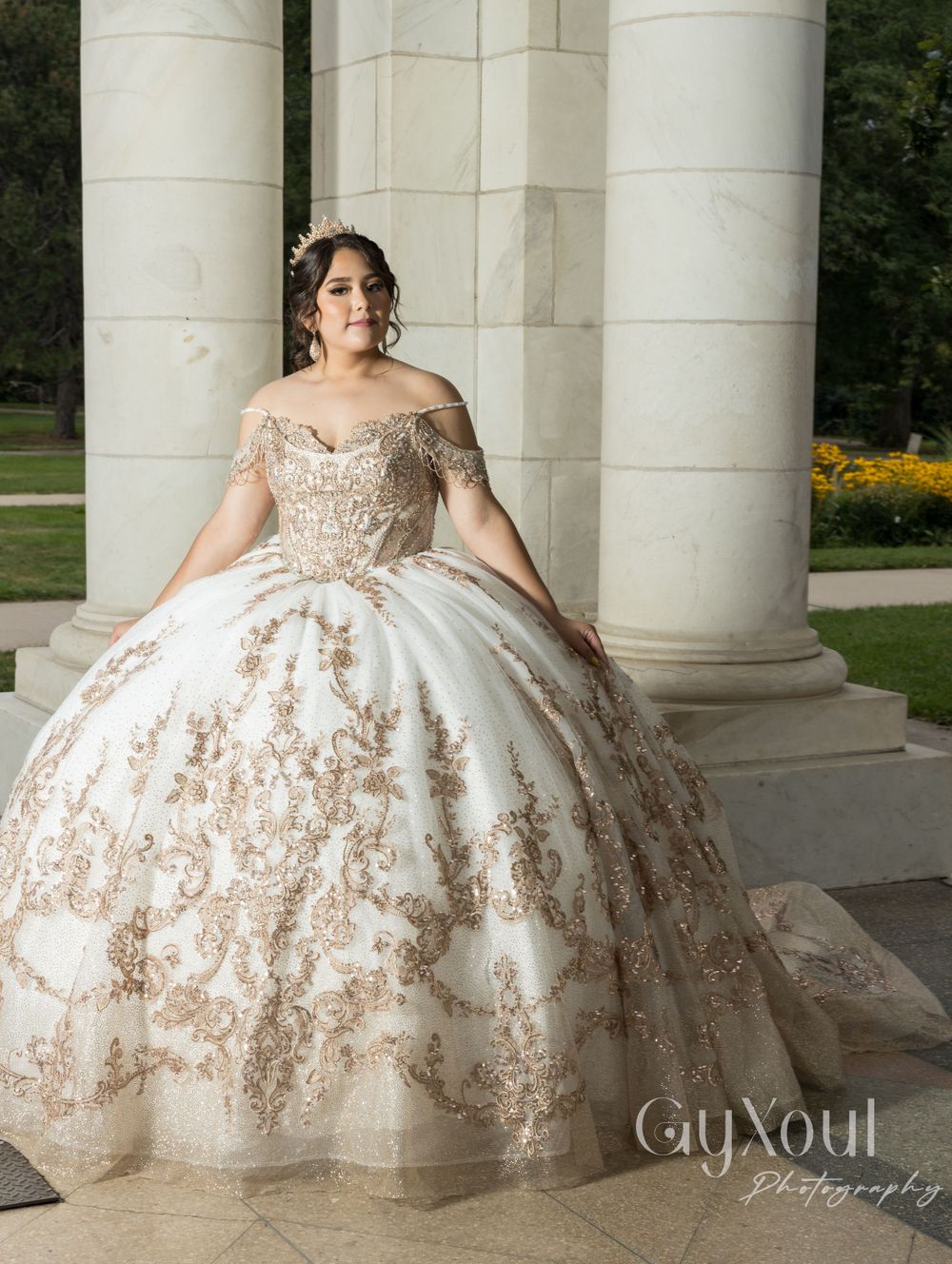 A detailed shot of an off-shoulder quinceañera gown with intricate gold embroidery and full tulle skirt.