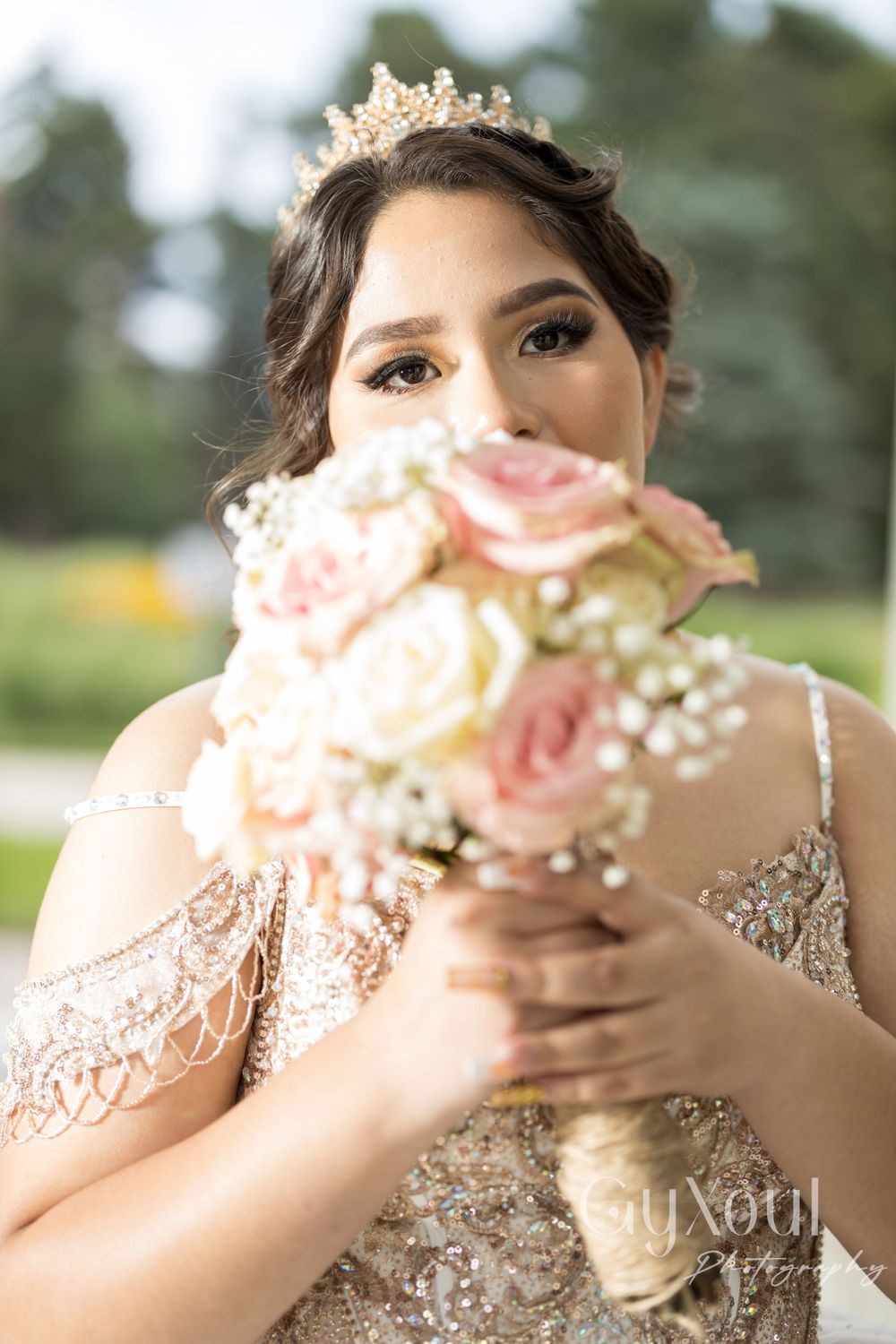 A close-up portrait showing a bouquet of pink and cream roses with a gold crown accessory.