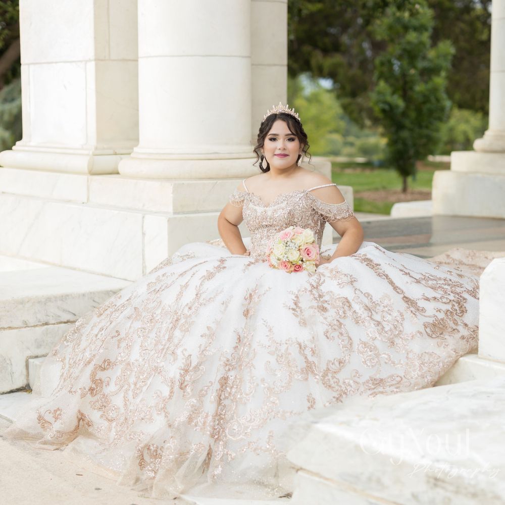 A quinceañera in a champagne-colored lace gown sits gracefully on white stone steps.