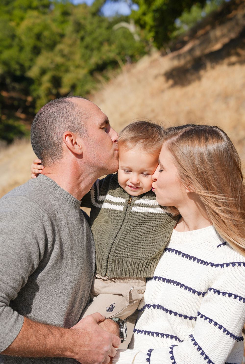 A tender family moment captured outdoors with soft natural lighting and warm expressions.