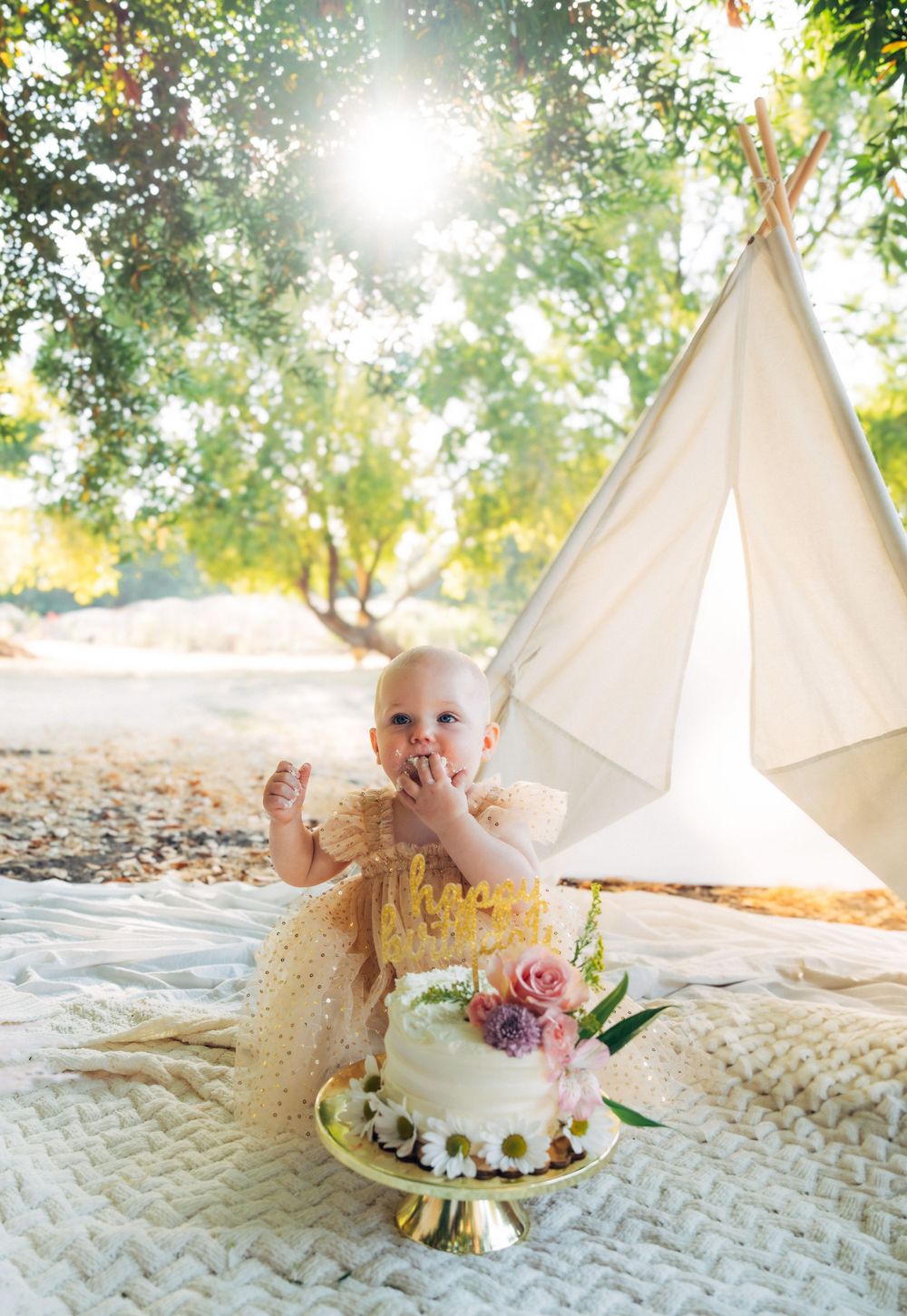 A cake smash photoshoot sequence showing a white floral cake on a gold stand against a light teepee backdrop outdoors.