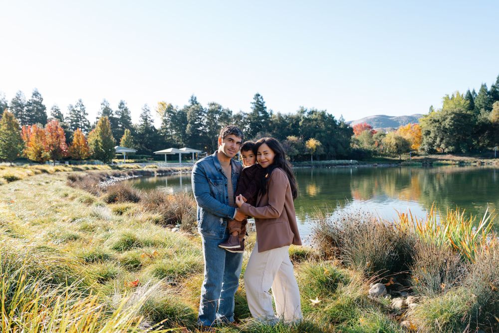 Family stands together by scenic lake with mountains in background.