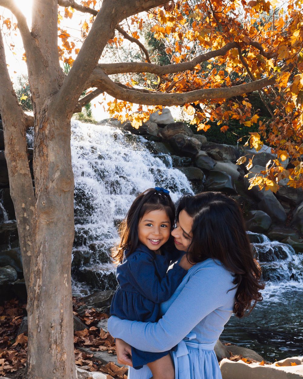 A joyful moment shared by two people embracing near a cascading waterfall with autumn foliage in the background.