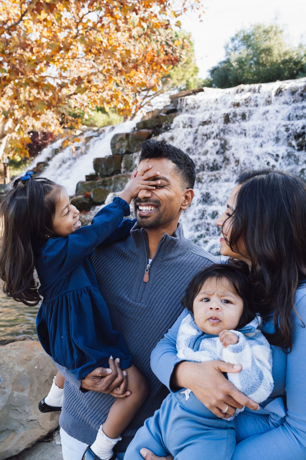 A family shares a playful moment together by a waterfall on an autumn day at Bollinger Canyon Fountain in San Ramon, California