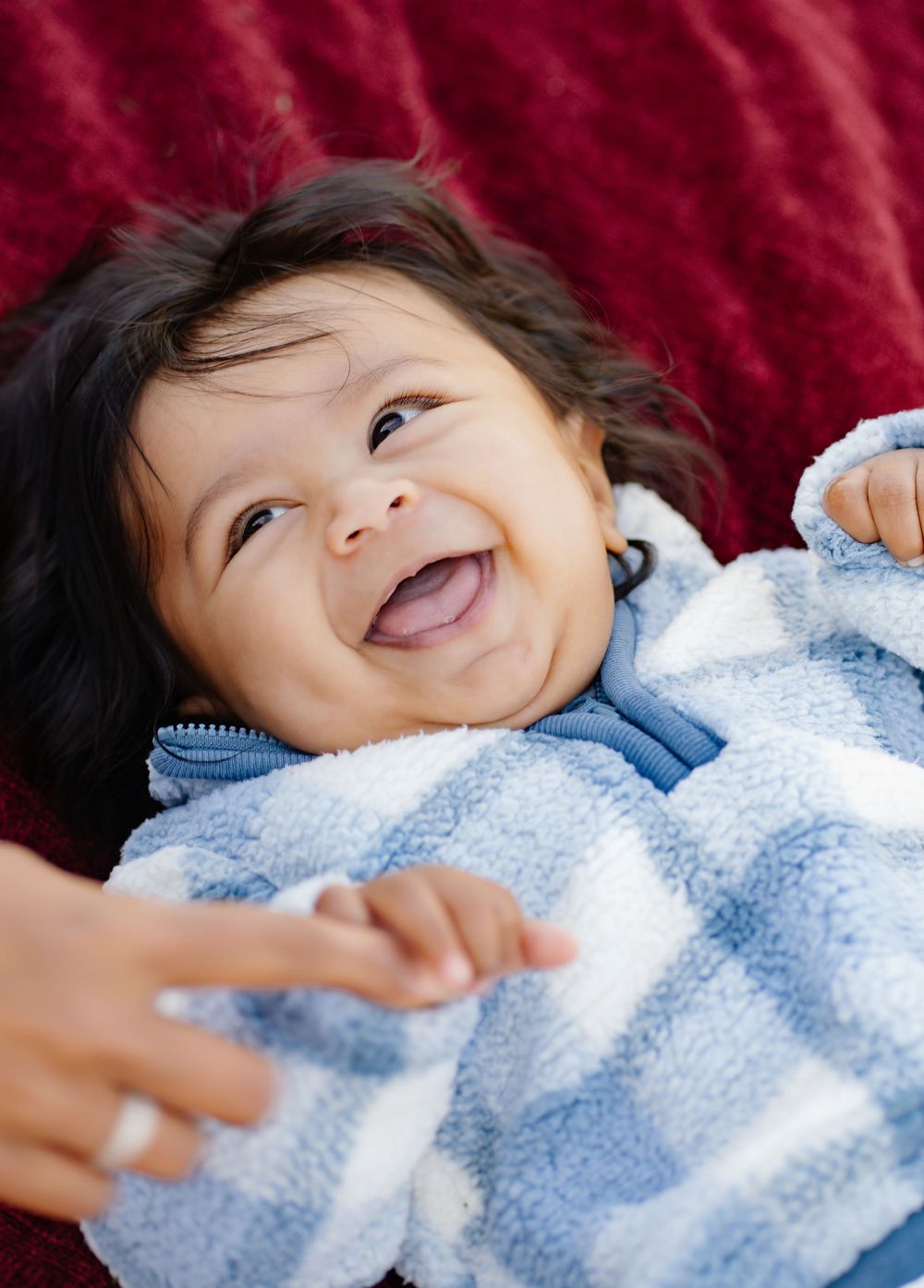 Happy baby wearing a blue blanket smiles with joy while lying on a red background.