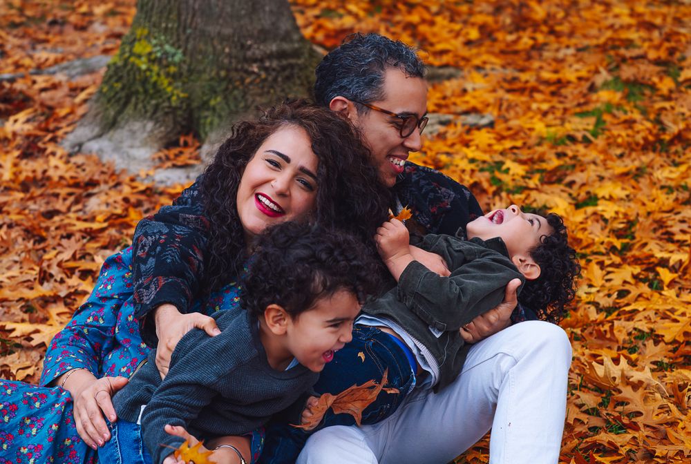 Joyful family plays together on fallen autumn leaves during an outdoor photoshoot in warm fall colors.
