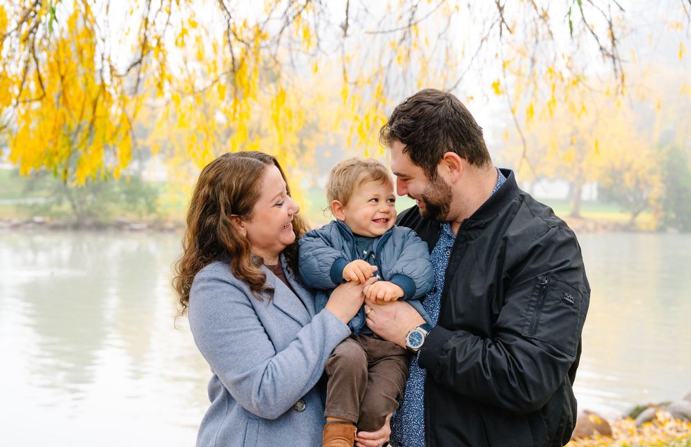 Family shares a joyful moment together near a tranquil lake with golden autumn willow trees in the background.