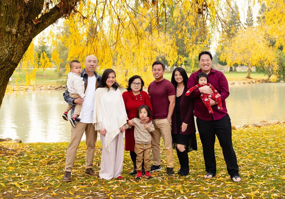 Group stands together on fallen autumn leaves by a lake with golden trees in the background.