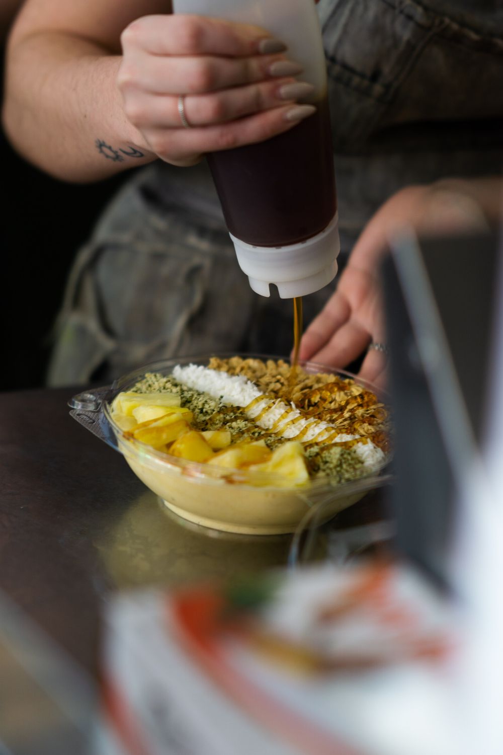 A sequence of photos showing hands sprinkling toppings onto a creamy dessert bowl with yellow fruit garnish.
