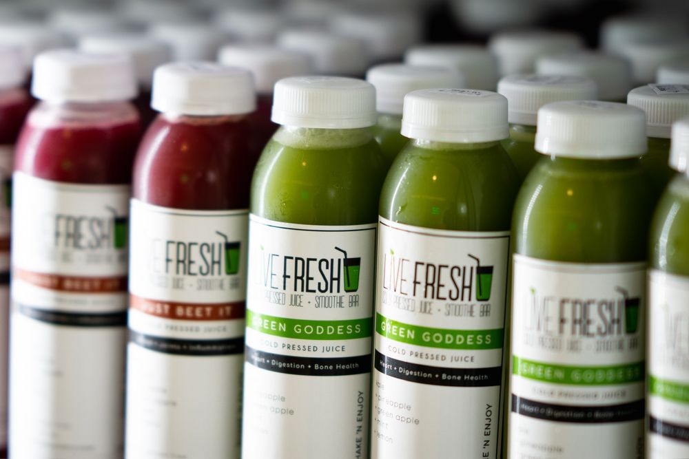 Rows of fresh cold-pressed juice bottles in green and white colors displayed on refrigerated shelves.