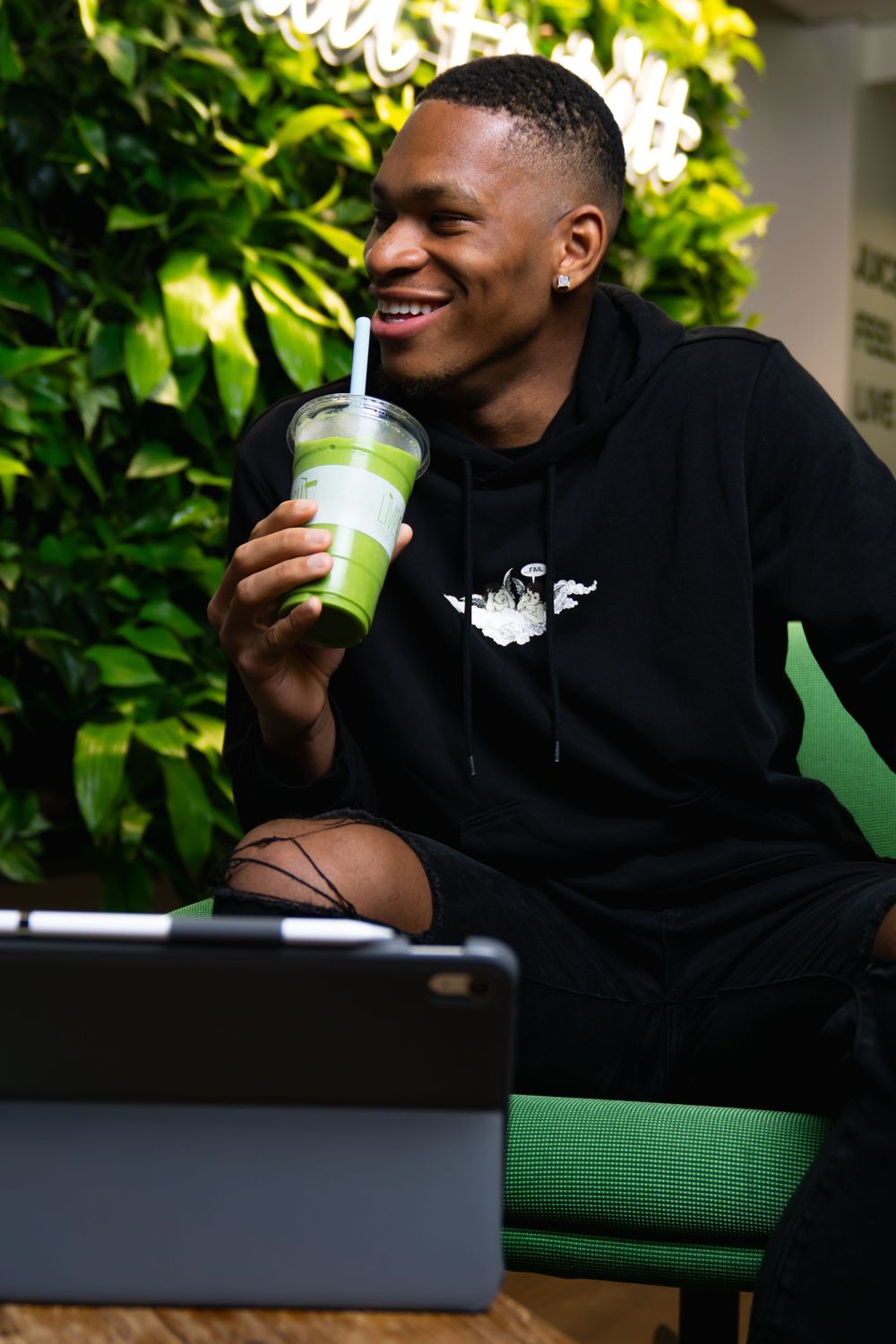 Person in black hoodie relaxes on green cushion while enjoying a refreshing drink from a lime green tumbler.
