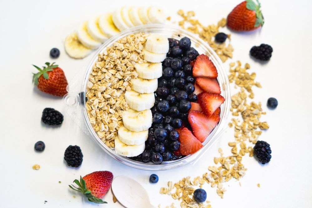 Fresh yogurt bowls topped with sliced bananas, berries and granola arranged in a row on white background.
