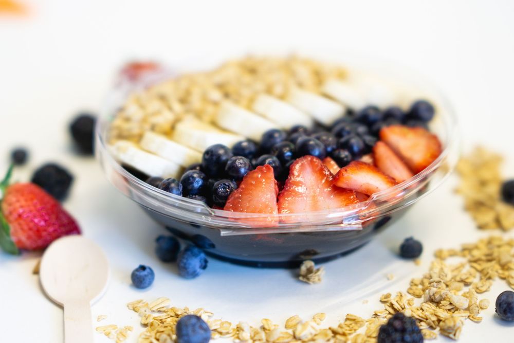 Fresh berries and granola arranged on white surface with yogurt parfait bowls in background.