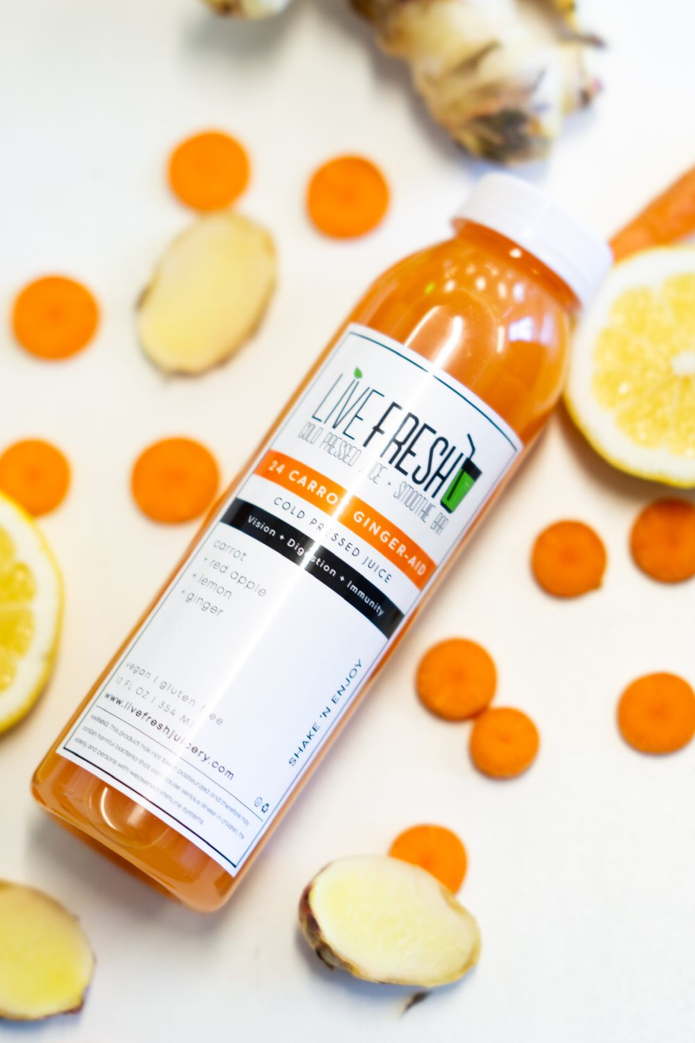Orange juice bottles and sliced ginger arranged with citrus fruit on a white surface.