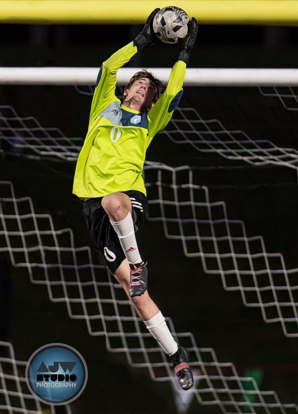 Goalkeeper in neon yellow jersey making dramatic save leap during night game.