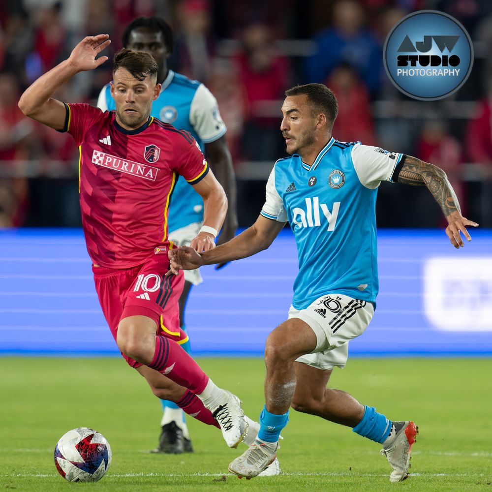 Two MLS soccer players in contrasting jerseys compete for possession during a match.