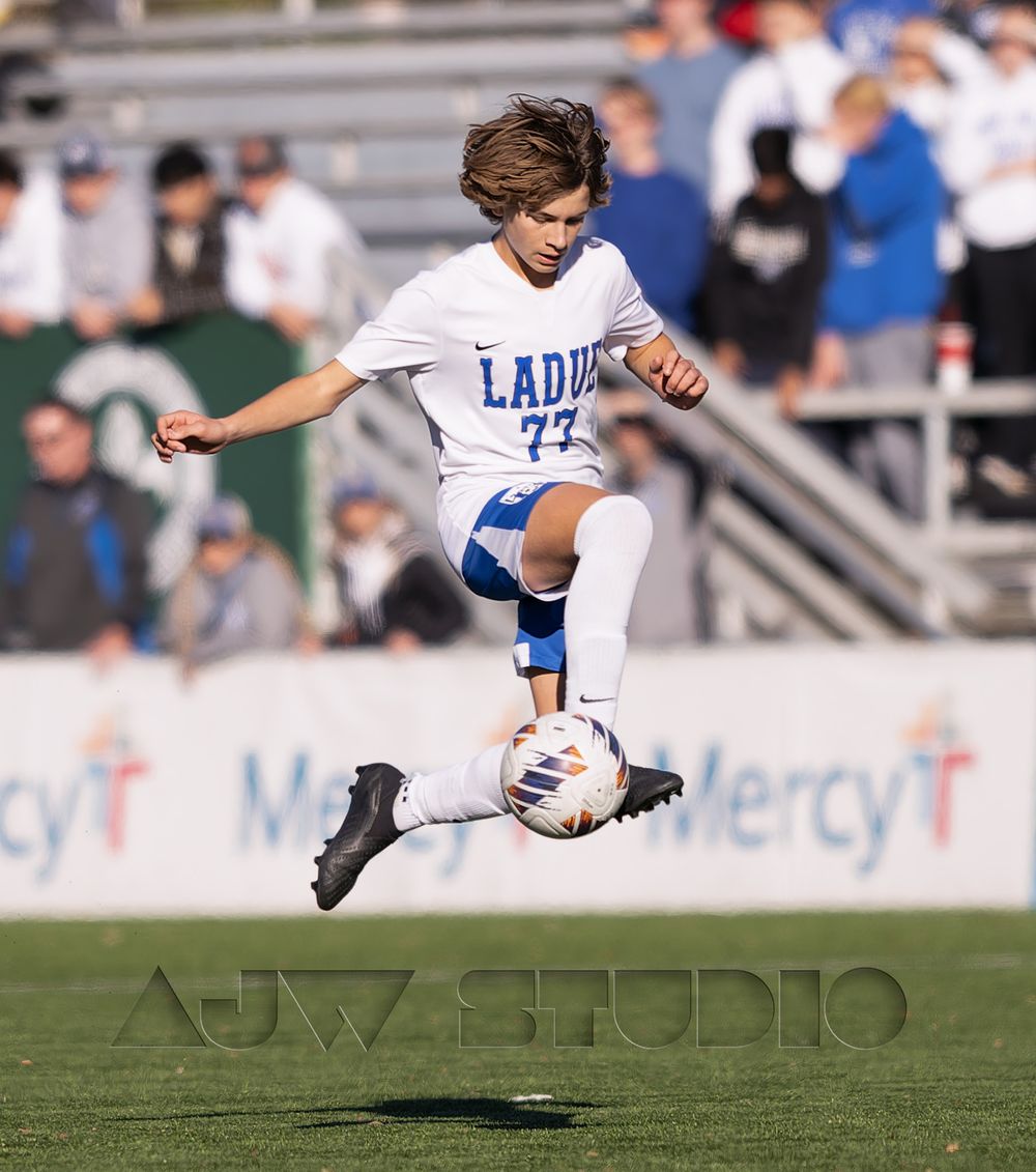 Youth soccer player performs aerial ball control in blue and white uniform.