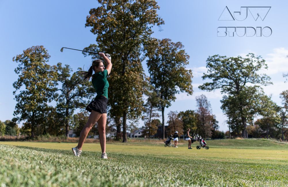 Golfer follows through on swing while competing on a sunny golf course.