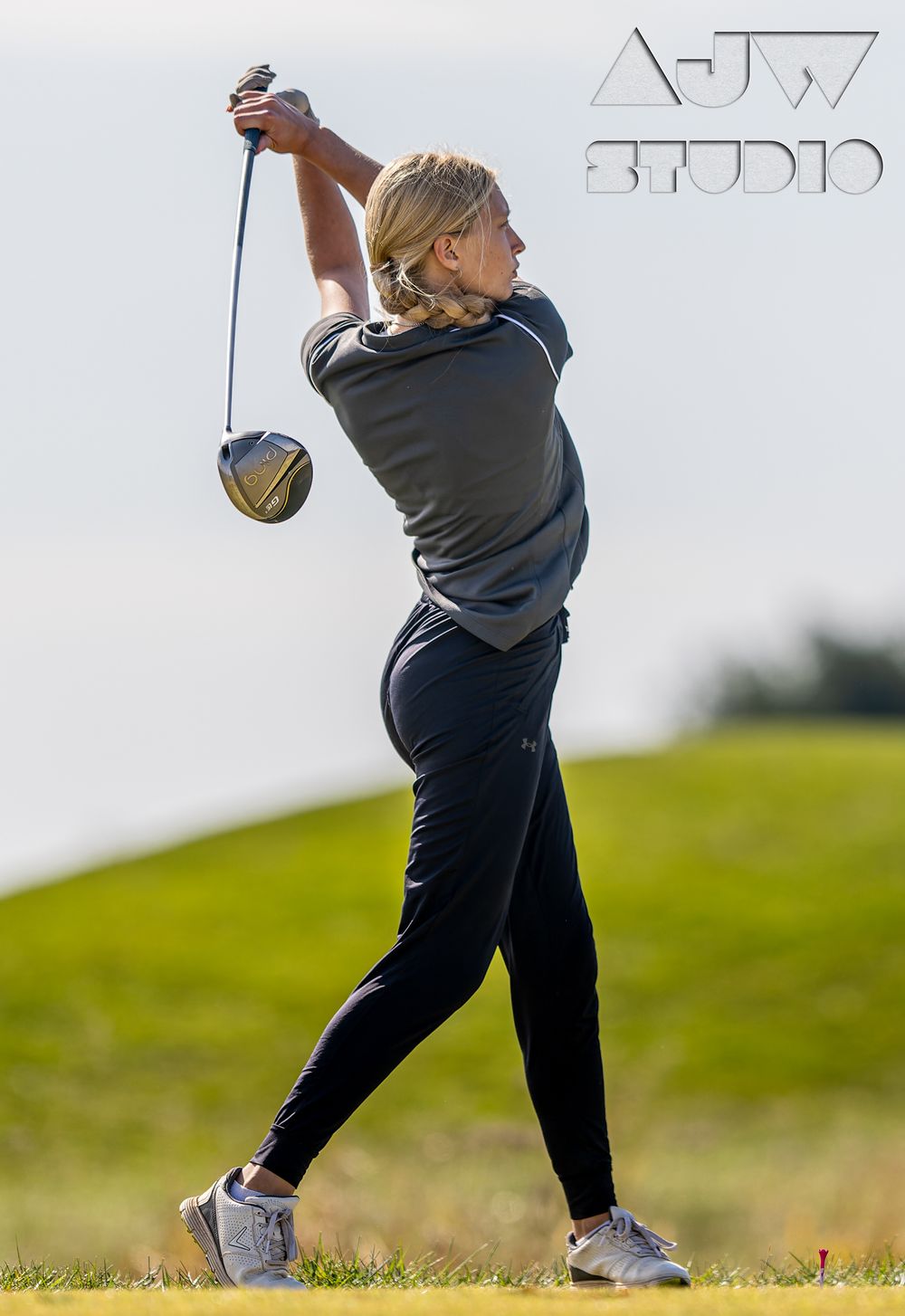 Golfer in grey attire displays full swing extension on rolling hill.