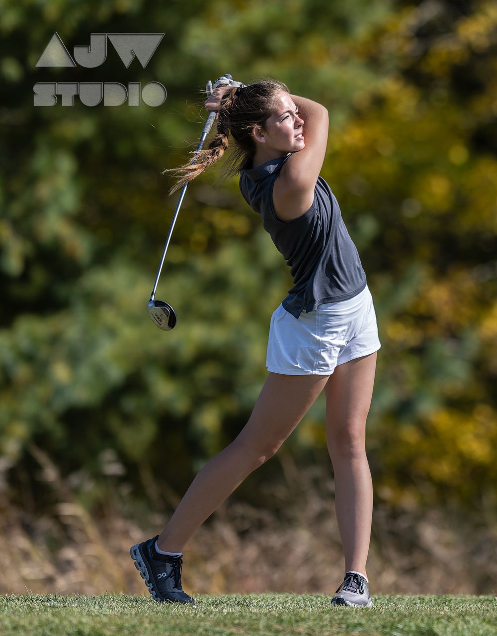 Athletic swing captured mid-motion on sunny golf course with autumn foliage background.