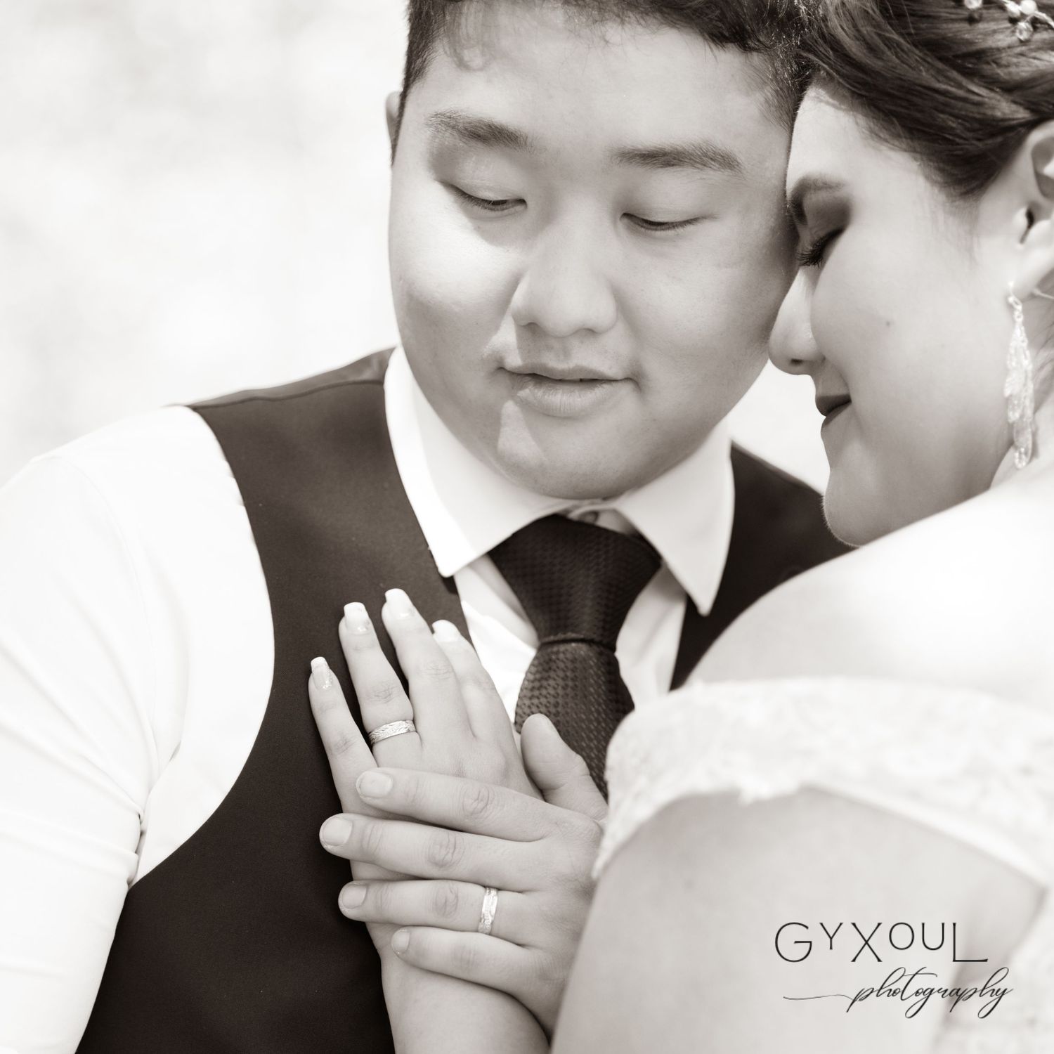 A romantic black and white wedding photo showing hands with rings touching in an intimate moment.