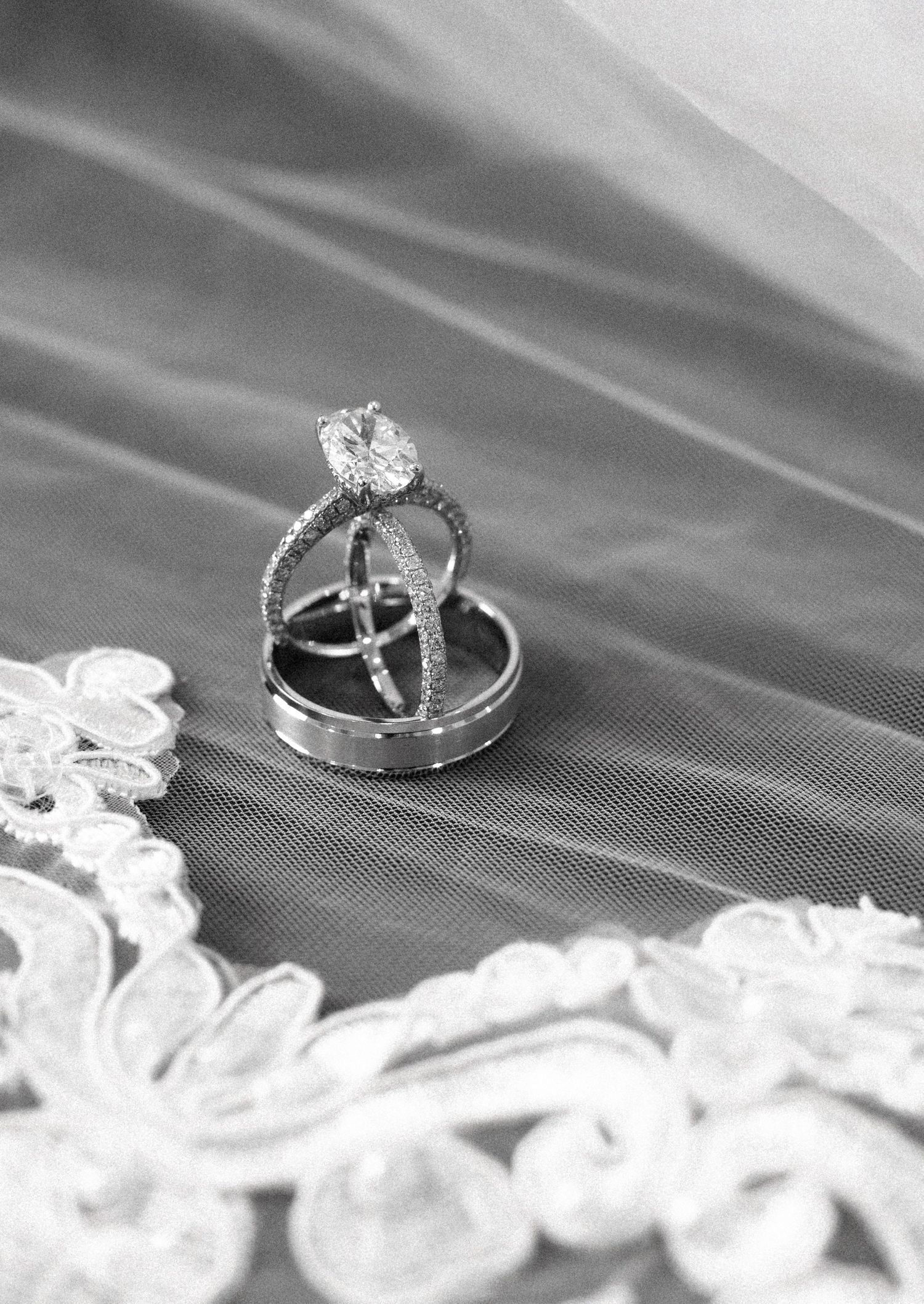 Black and white photograph of wedding rings with a large diamond engagement ring nestled on lace details.