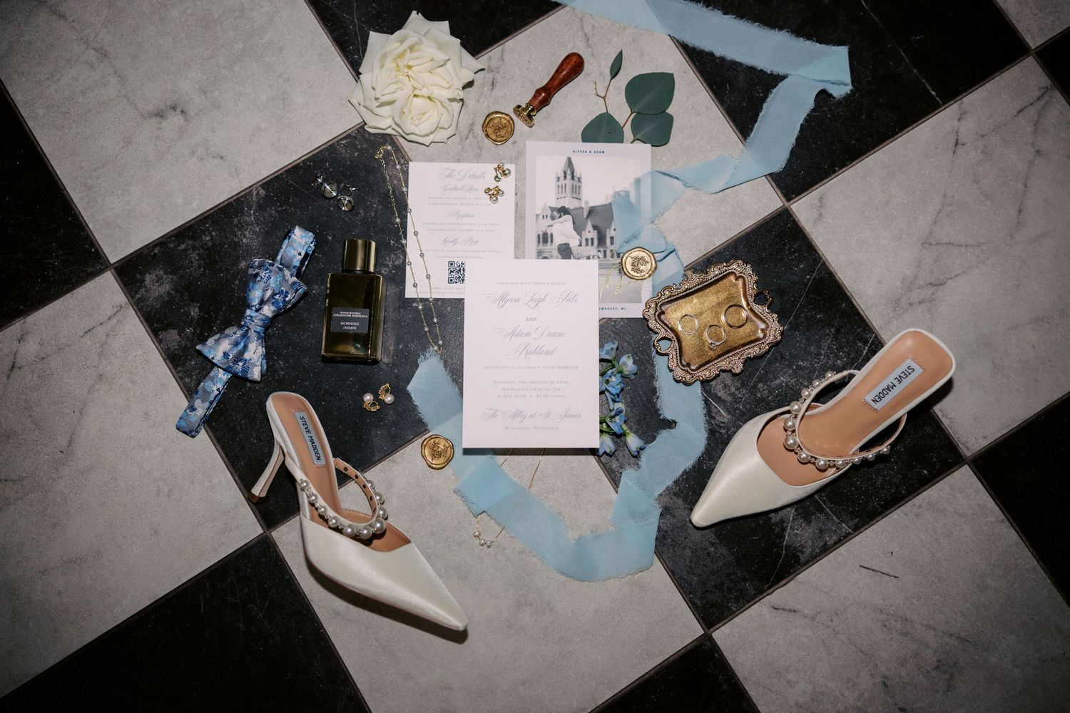 Wedding accessories including shoes, jewelry and invitations arranged on a black and white checkered floor.