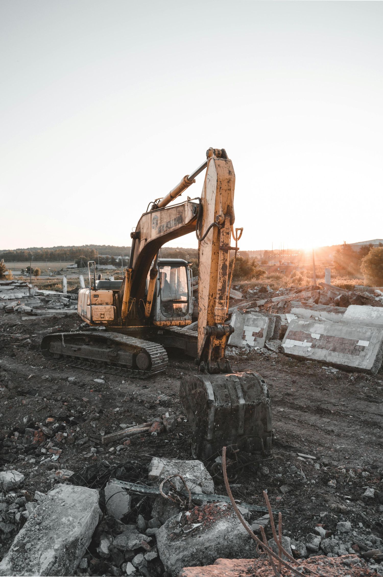 Excavator machine at construction site during sunset with rocky debris in foreground.