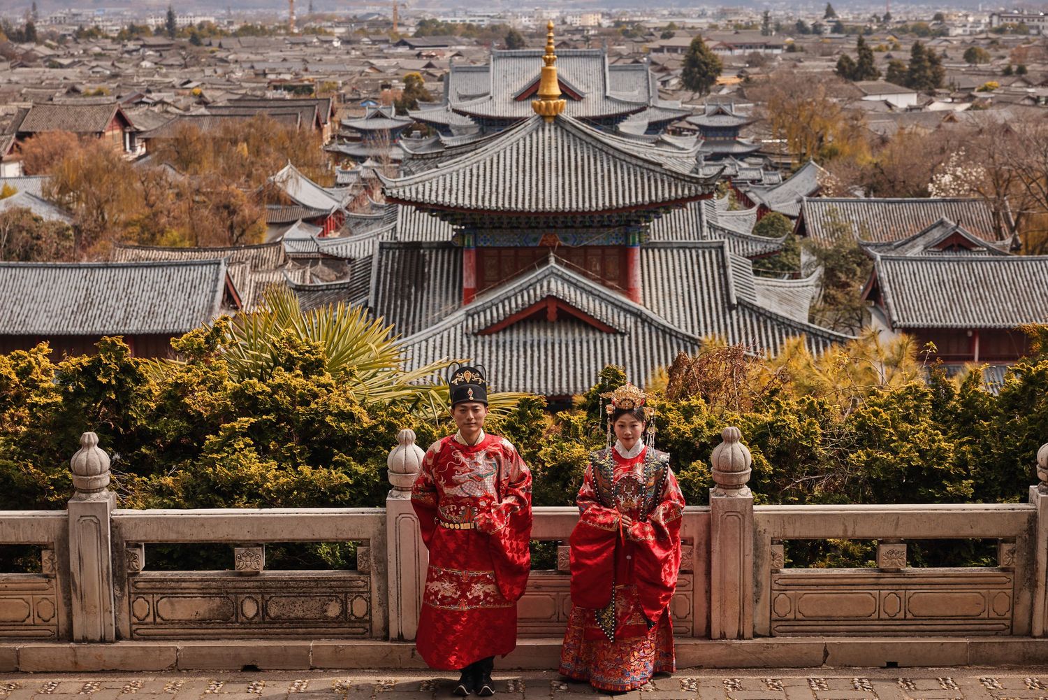 Traditional Chinese temple entrance with ornate roofs and dragon stone carvings on steps decorated with orange flowers.