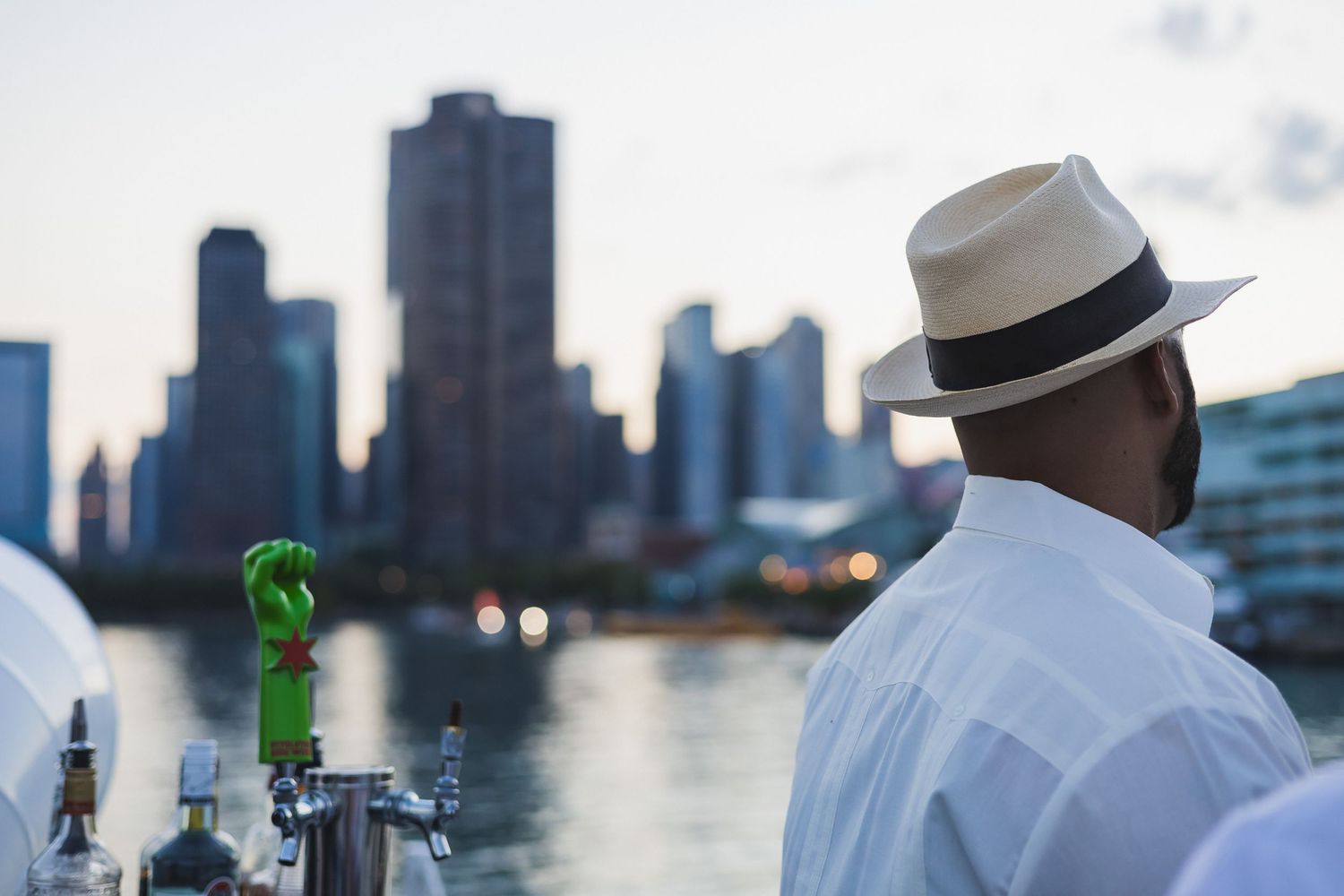 Person in white shirt and hat looking at city skyline reflection on waterfront.