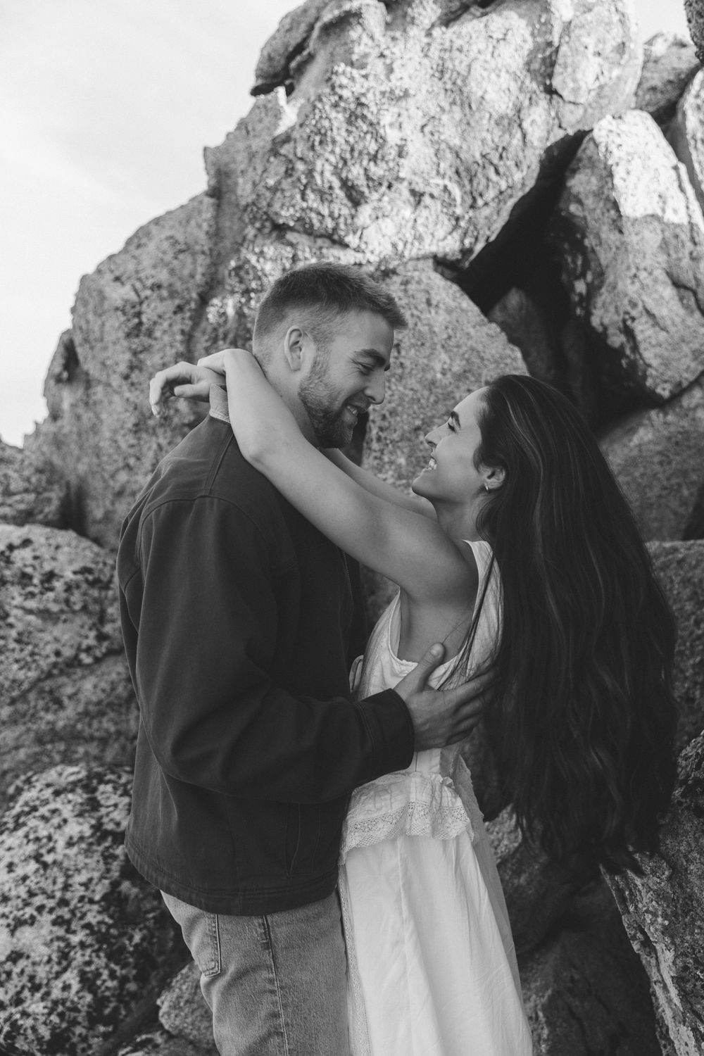 A romantic couple embraces against a rocky backdrop in a series of intimate black and white photos.