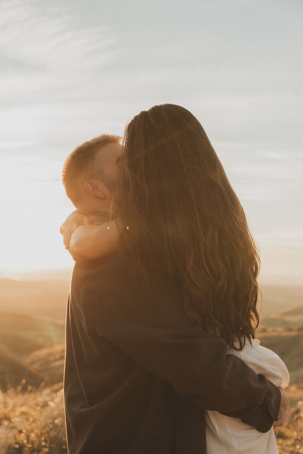 A romantic silhouette of a couple embracing in warm sunlight against a scenic landscape.