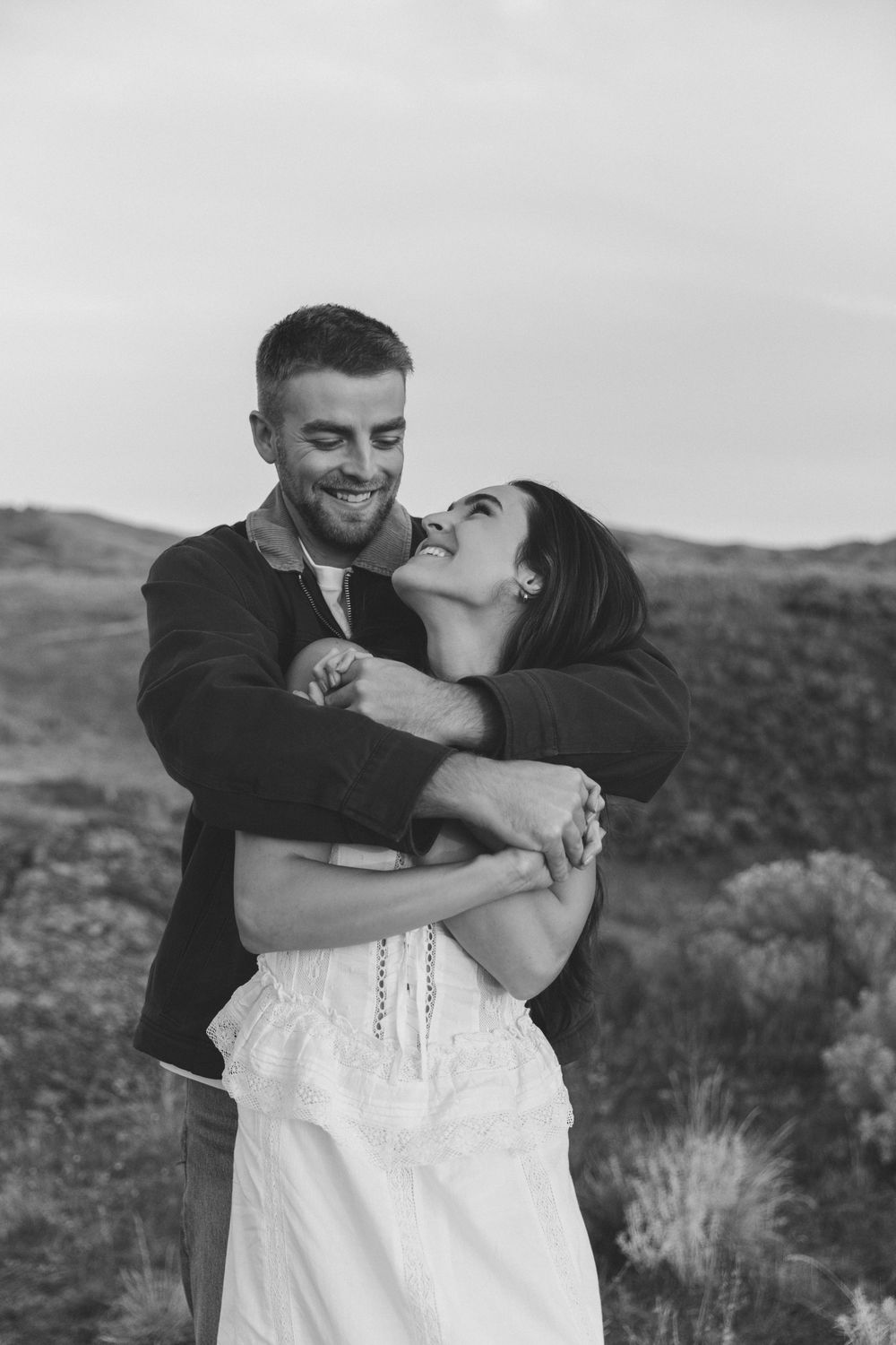 A romantic couple embraces and shares a tender kiss in a desert landscape at sunset.