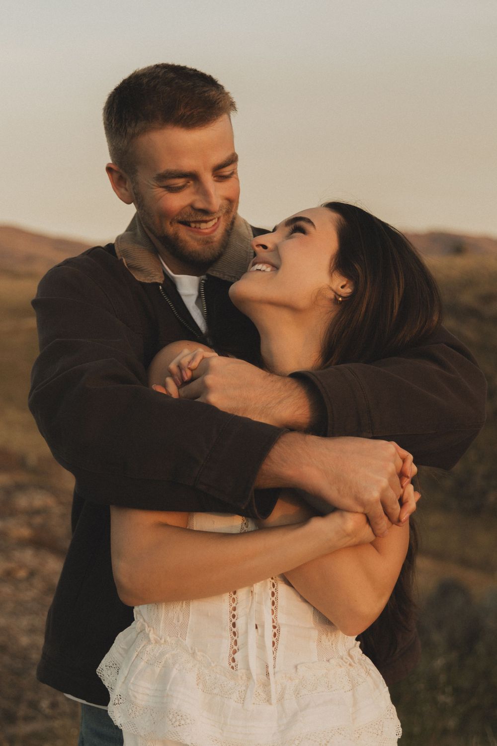 Romantic couple embracing and laughing together during golden hour in a desert landscape setting.