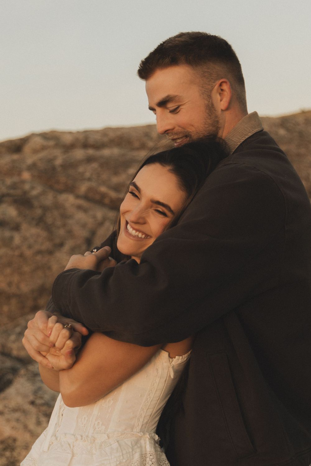 Intimate couple sharing a tender moment while embracing against a desert mountain backdrop at sunset.