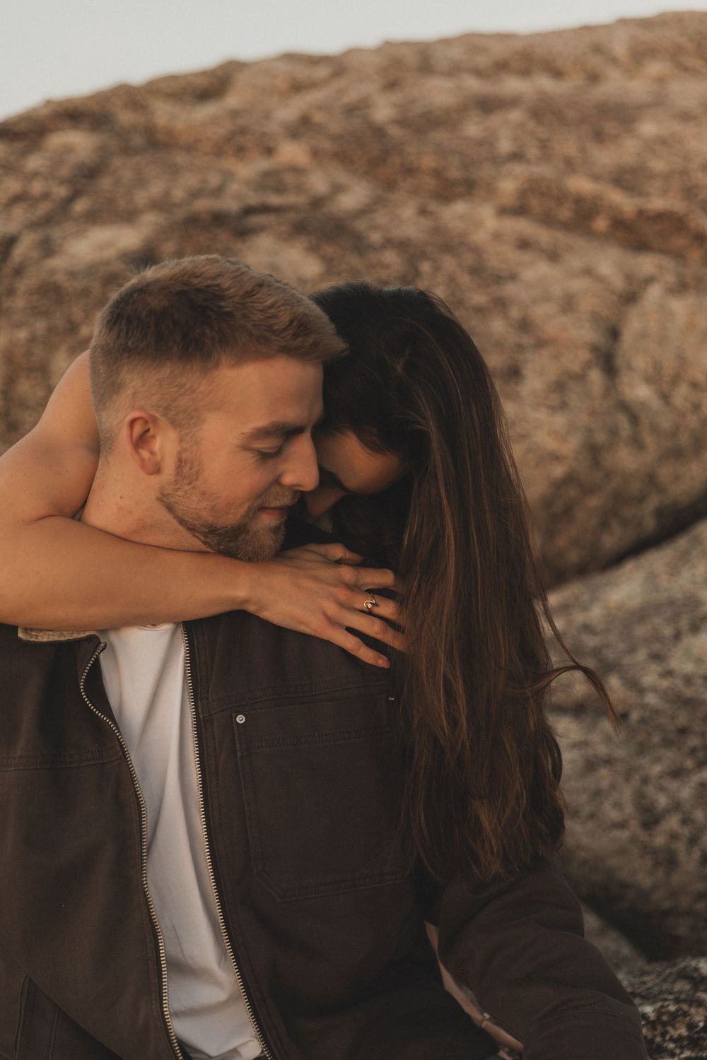 Romantic couple sharing intimate moments against a rocky backdrop at sunset.
