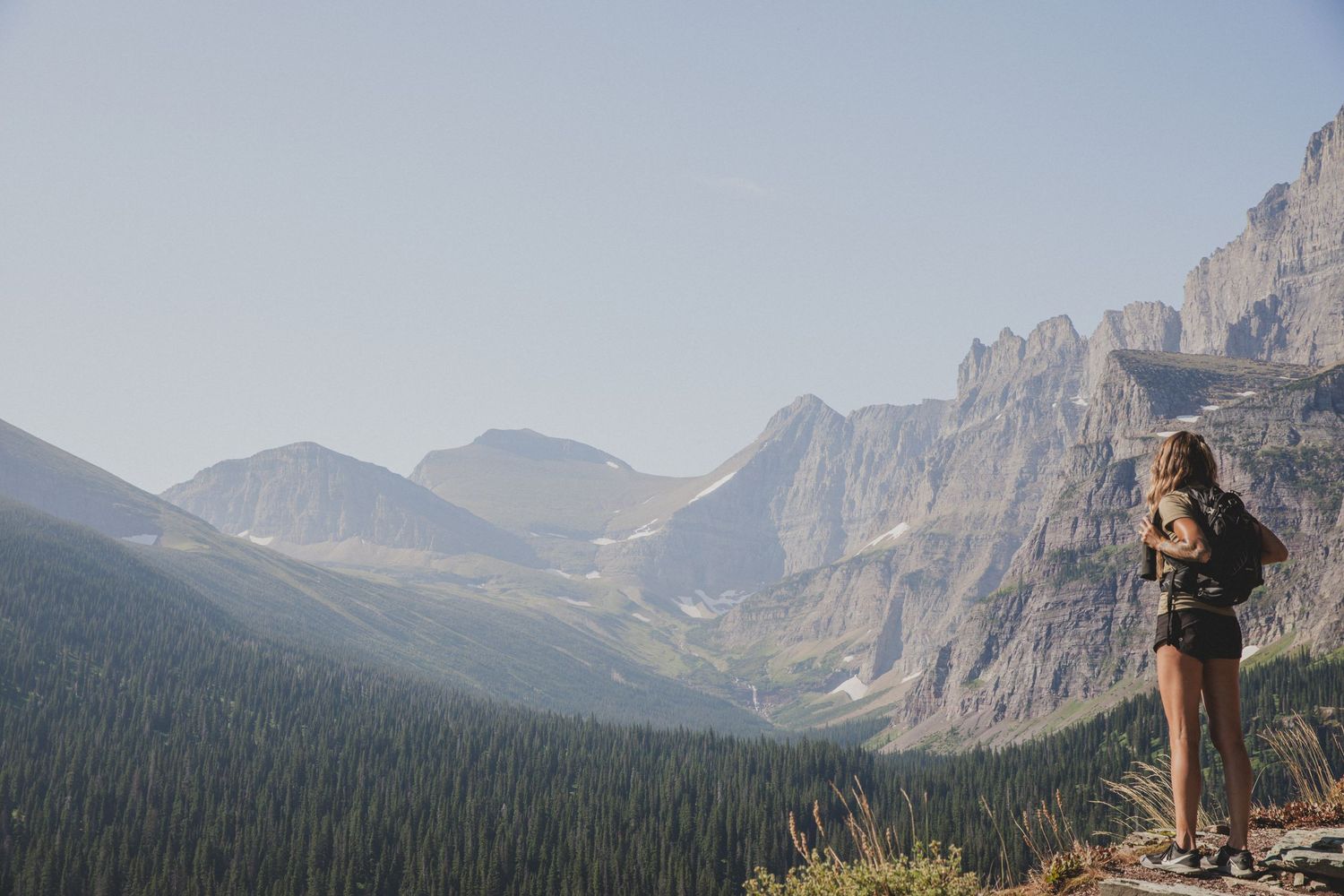 Hiker overlooking a vast mountain valley with dramatic rocky peaks in the distance.